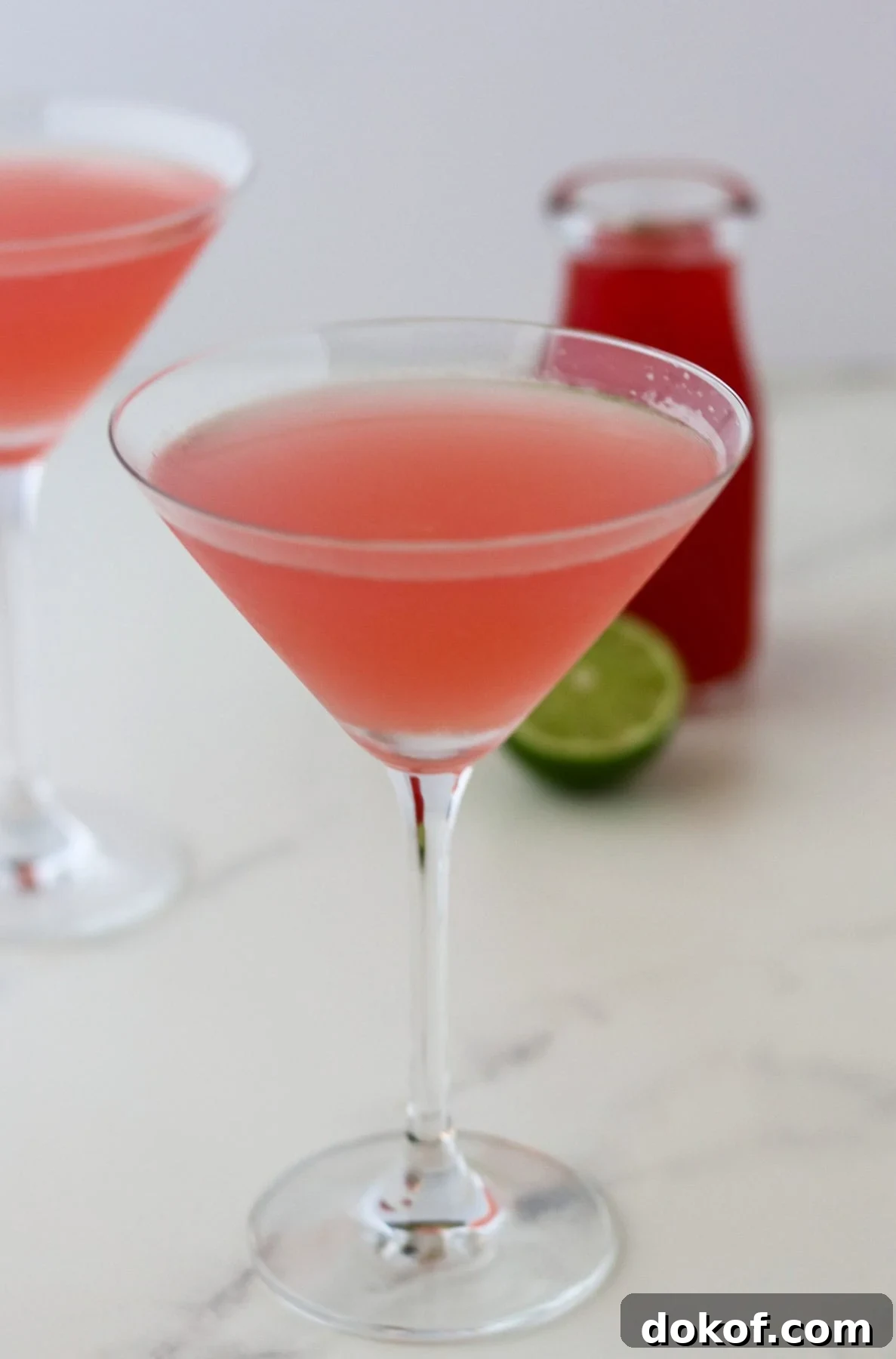 Rhubarb cocktail in a martini glass next to a lime and bottle of rhubarb syrup (cordial).