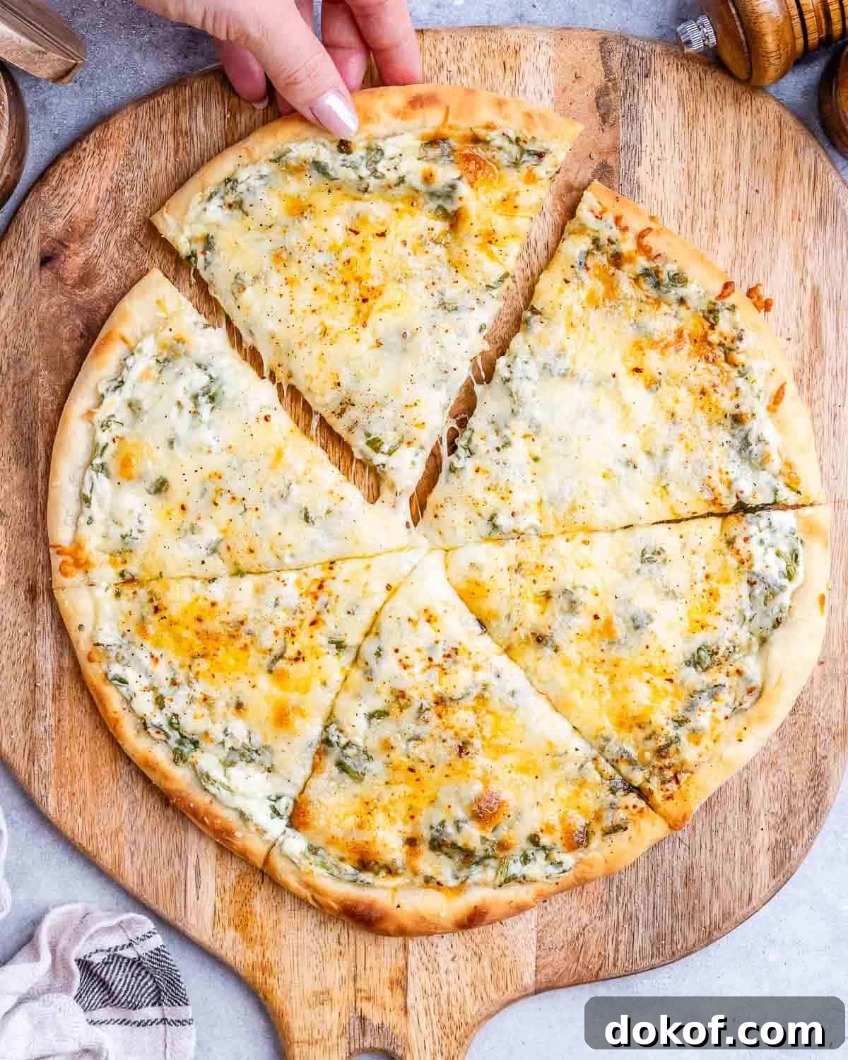 High-Protein White Pizza Recipe for Muscle Building 2 A white pizza sliced into 6 slices on a wooden board with a hand pulling one slice away.