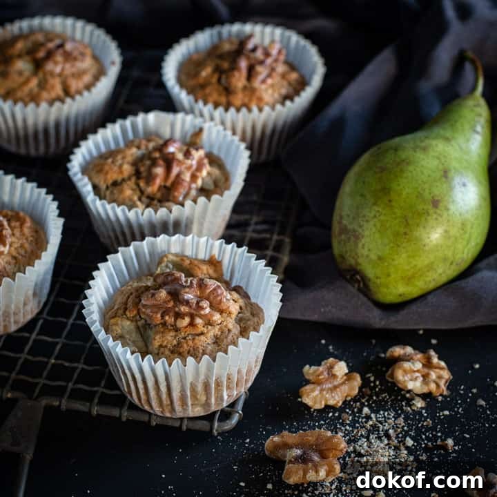 black background and 5 pear muffins on a rustic cooling rack with raw green pears and walnut halves scattered around