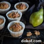 black background and 5 pear muffins on a rustic cooling rack with raw green pears and walnut halves scattered around