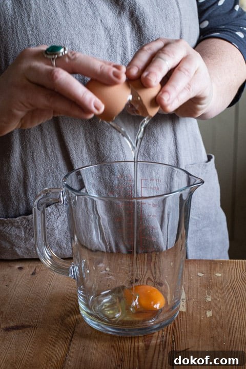 womans hands cracking an egg into a glass jug on a wooden kitchen counter