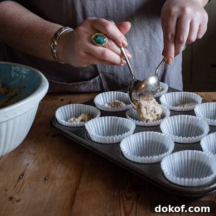 womans hands spooning pear muffin mixture into white paper muffin cases in a silver metal muffin tray