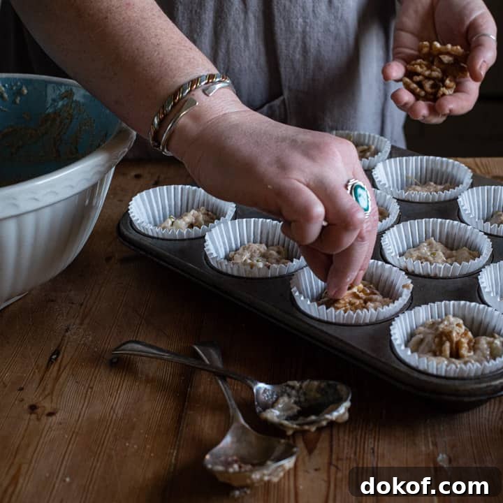 womans hands placing a wlnut half on top on a tray of muffins