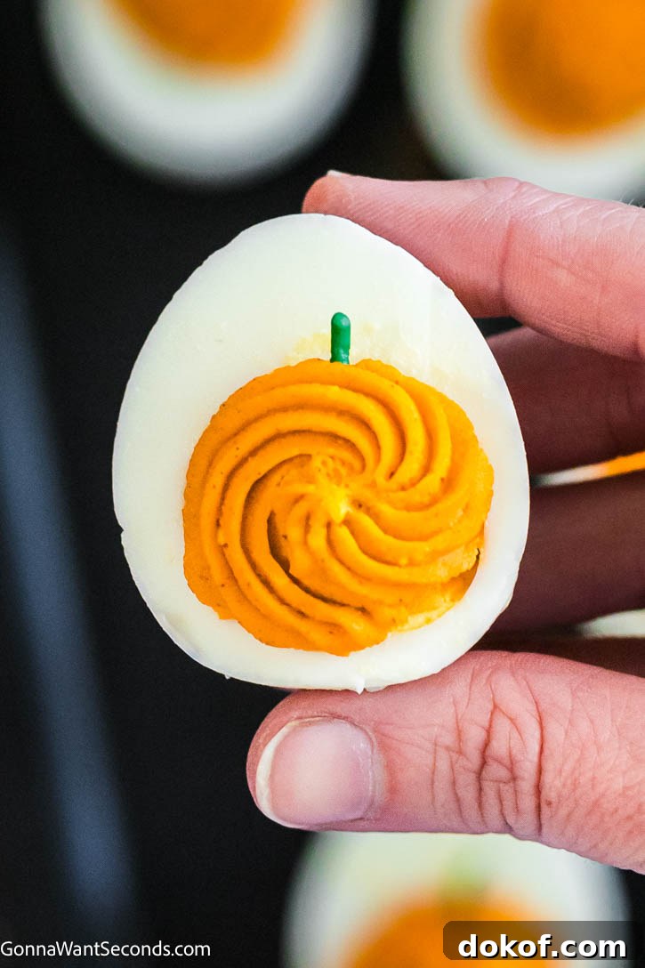 These spooky-cute Halloween Deviled Eggs have black-cracked shells and creamy orange filling. It's a stunning addition to any Halloween spread! #halloweenappetizers #deviledeggs hand holding halloween deviled egg close up