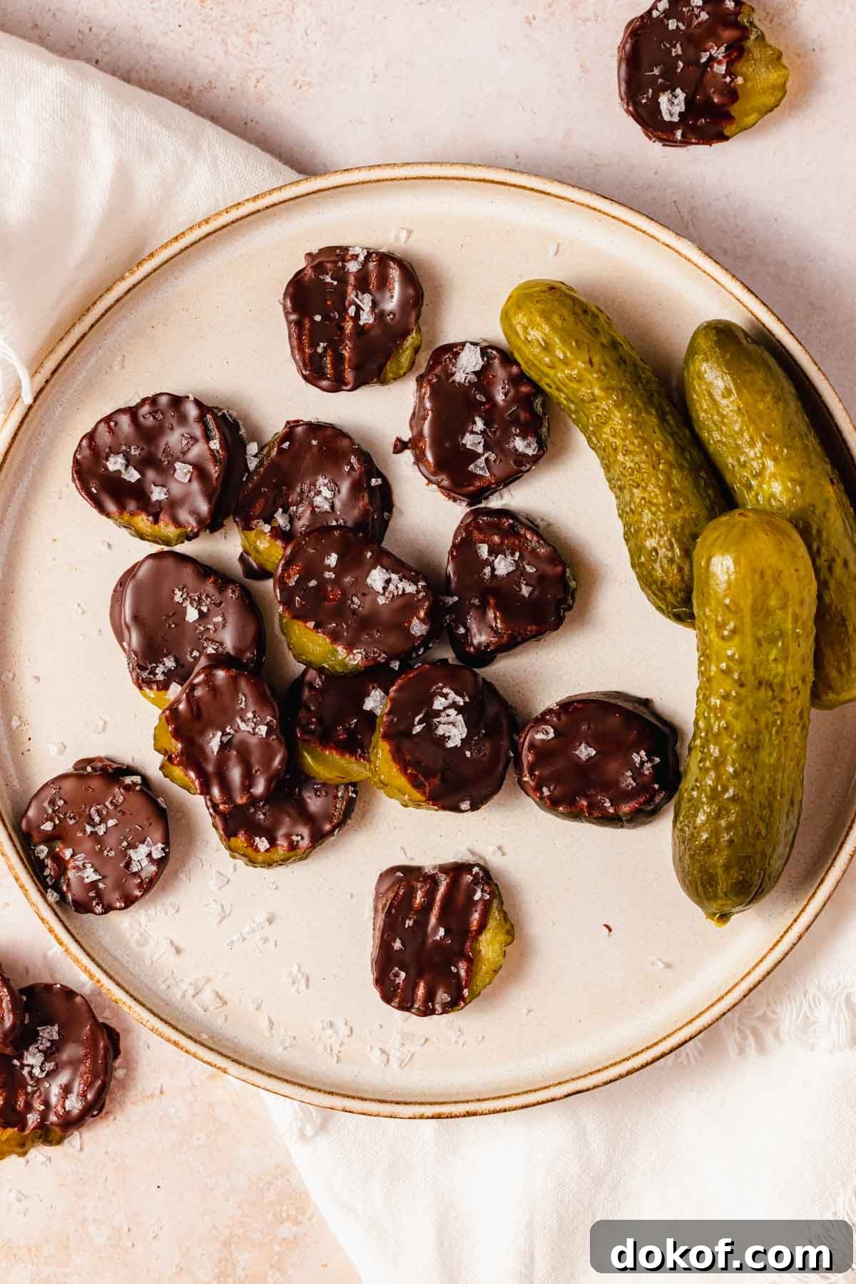 chocolate covered pickle slices with flaky salt on a plate with whole pickles on the side
