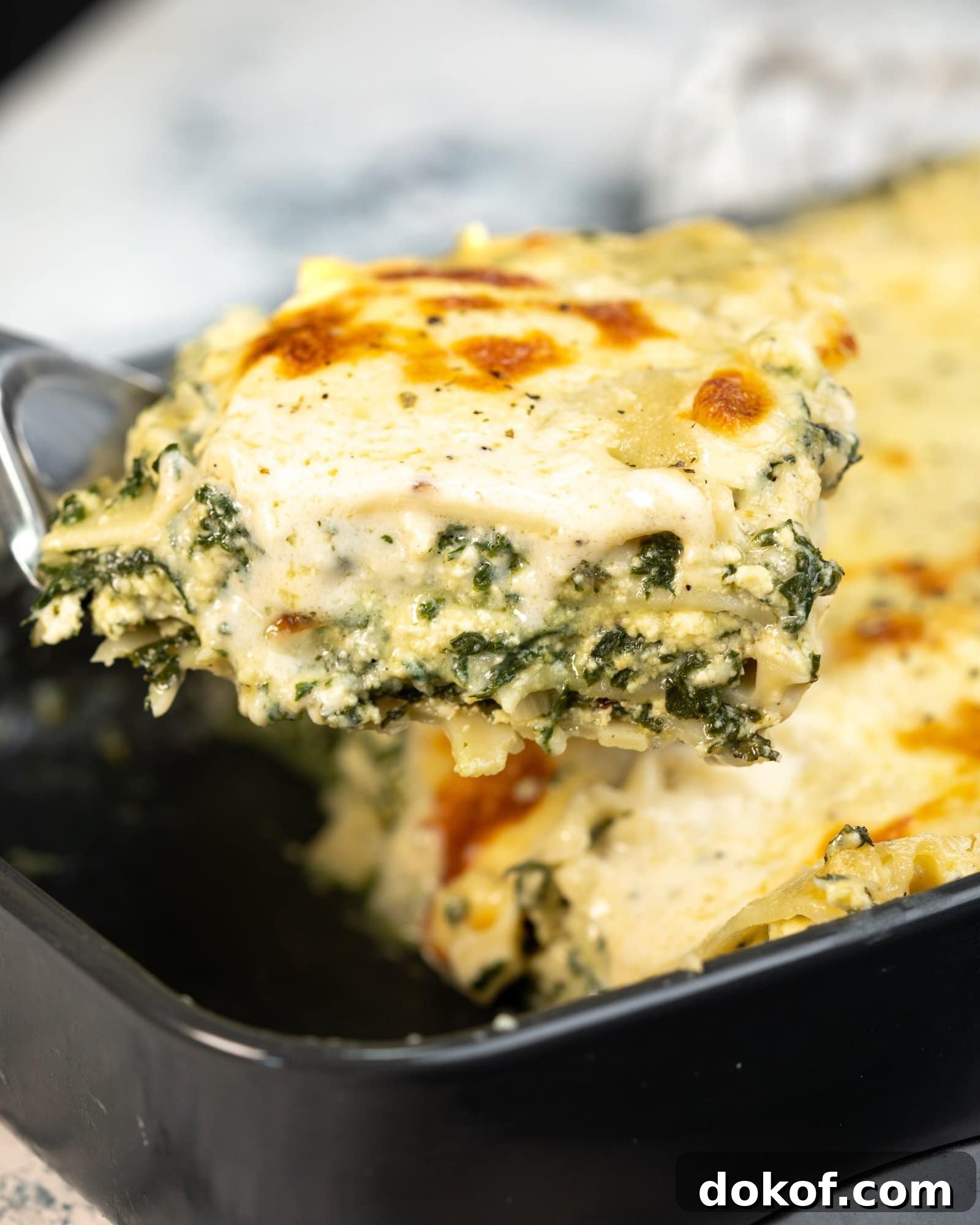 A slice of classic spinach lasagna picked up with a slotted spoon. The lasagna is creamy and cheesy between the layers with a white sauce.