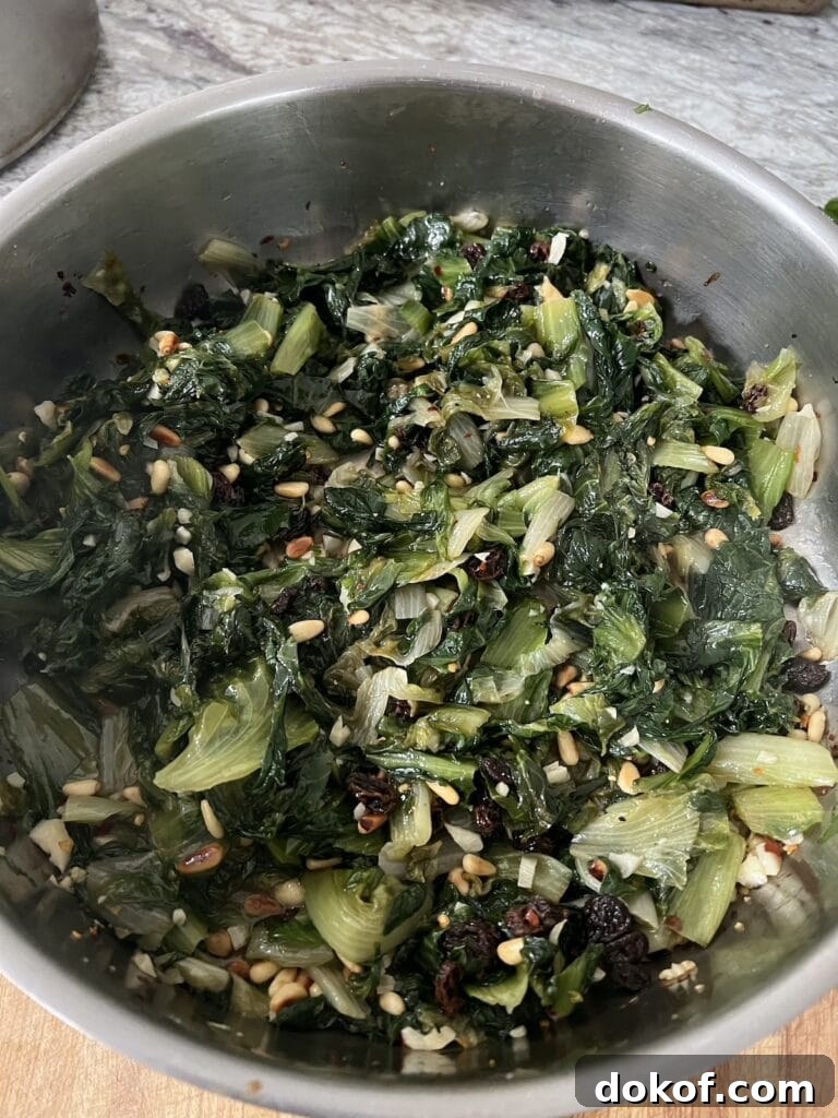 Sautéed Italian Escarole with pine nuts and raisins in stainless steel pan.