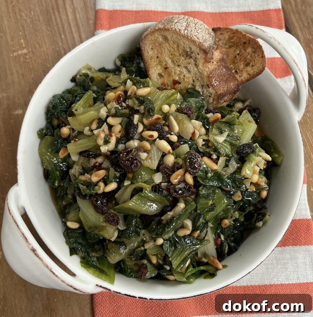 Sautéed Italian Escarole with pine nuts and raisins with 2 slices toasted bread in white dish over decorative towel