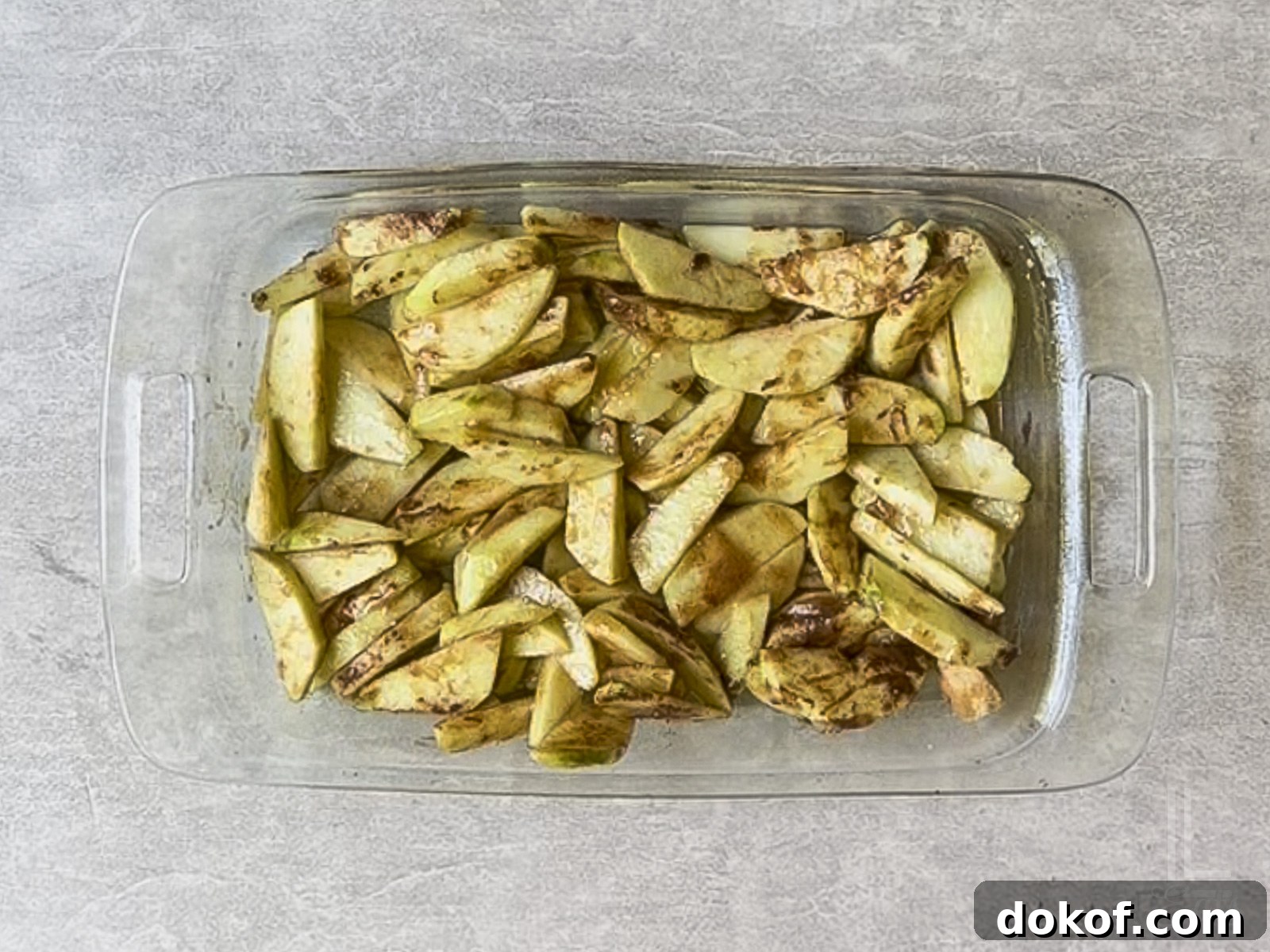 sliced apples covered with brown sugar, cinnamon, and butter in a glass baking dish.