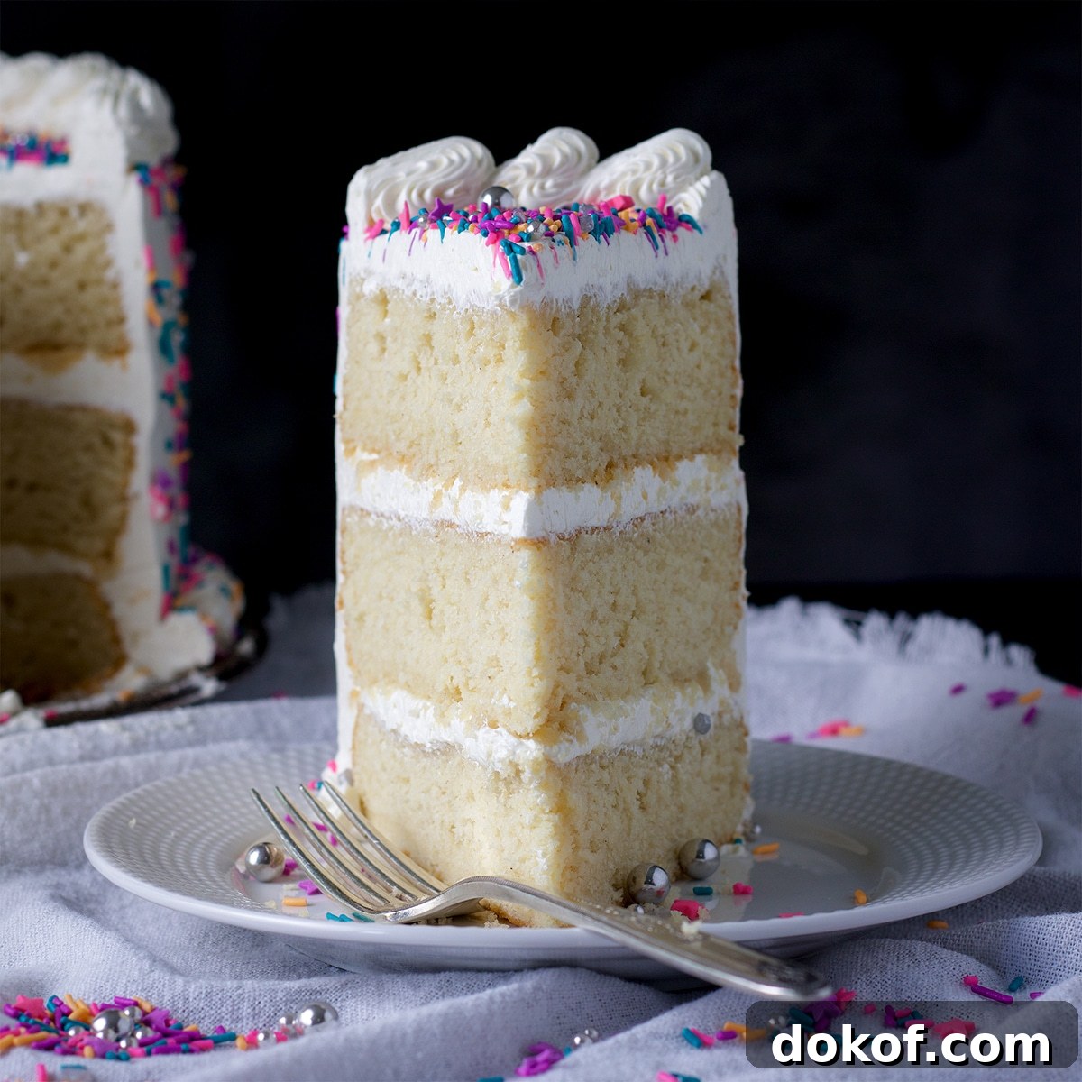 A slice of three layer gluten free vanilla cake frosted with buttercream.