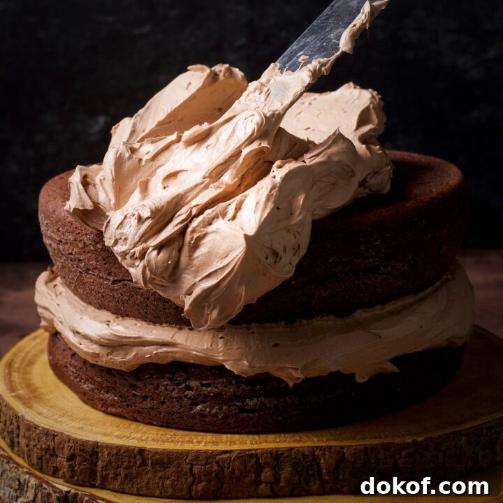 Someone using an offset icing spatula to spread milk chocolate buttercream.