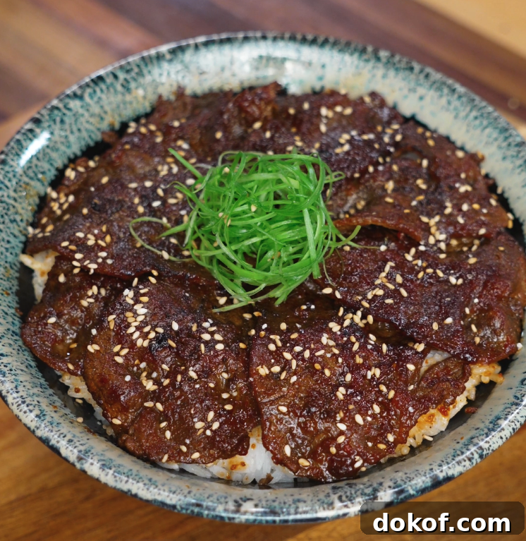 A bowl of Korean bulgogi beef served over white rice is topped with finely sliced scallions and toasted sesame seeds. The beef is glazed in a shiny sauce and arranged in a circular layer.