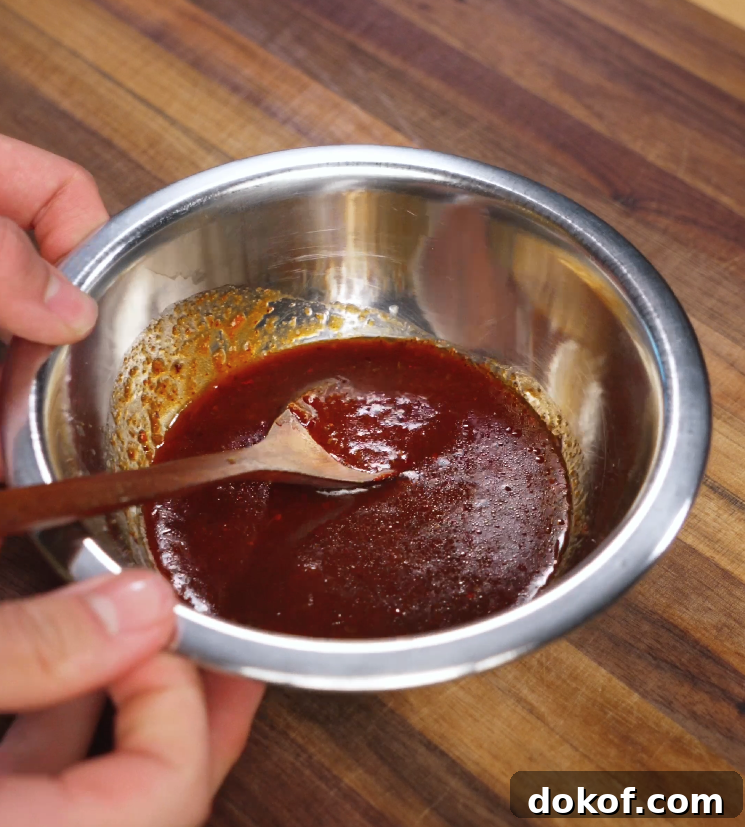 A wooden spoon is stirring a thick Korean bulgogi sauce inside a metal mixing bowl. The sauce has a rich reddish-brown color with a glossy texture, ready to coat the beef.