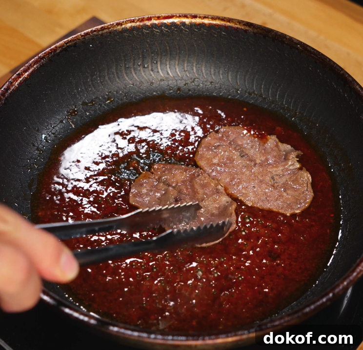 Thinly sliced beef is simmering in a bubbling sweet and savory bulgogi-style sauce in a skillet. The glossy sauce thickens around the meat, infusing it with deep umami flavor.