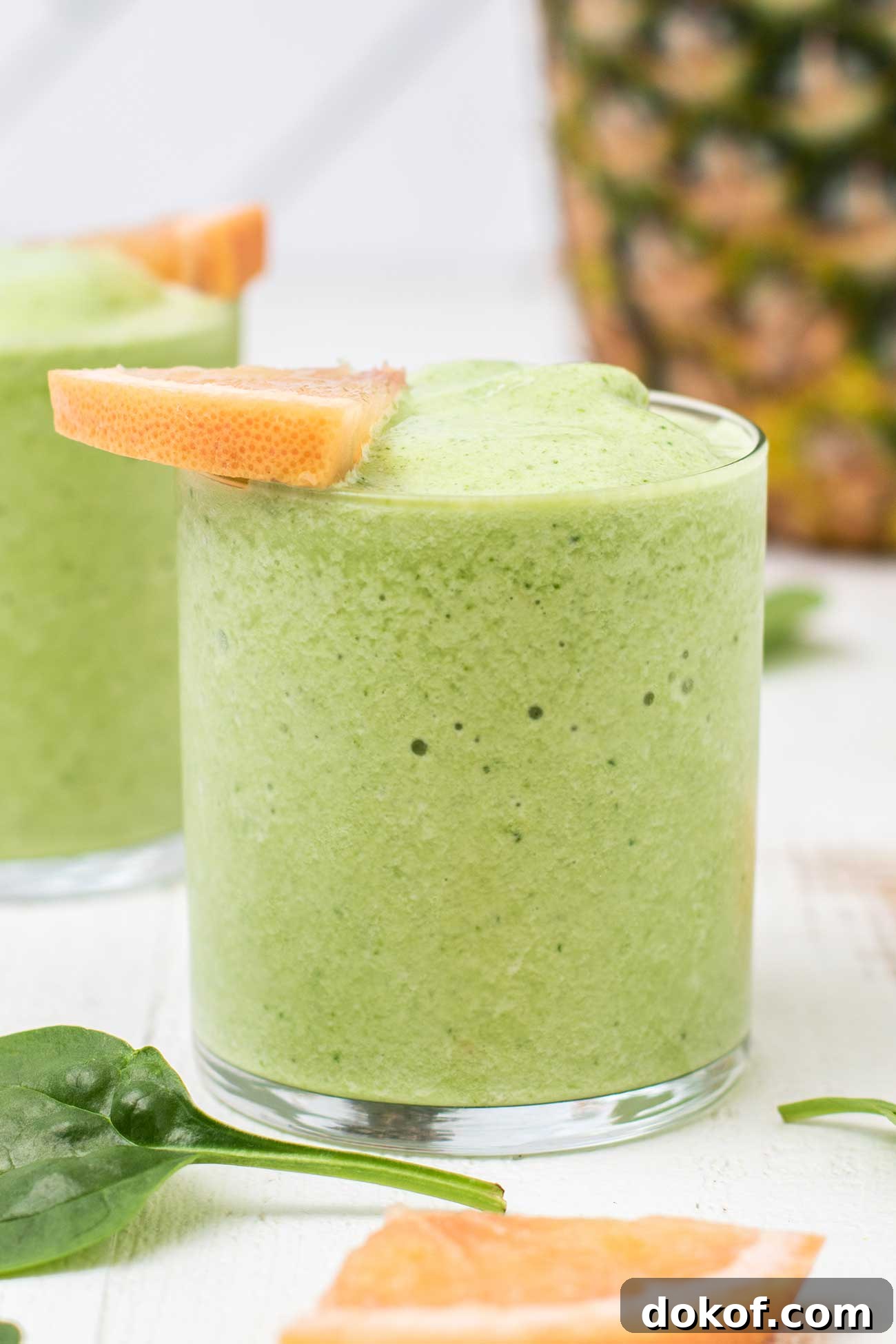 A vibrant green metabolism boosting smoothie in a glass garnished with a grapefruit slice.