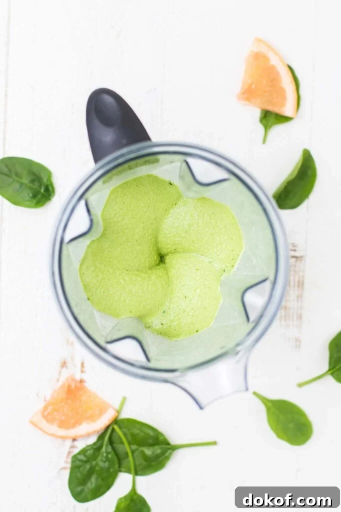 A bright green smoothie shown with a thick texture in a blender.