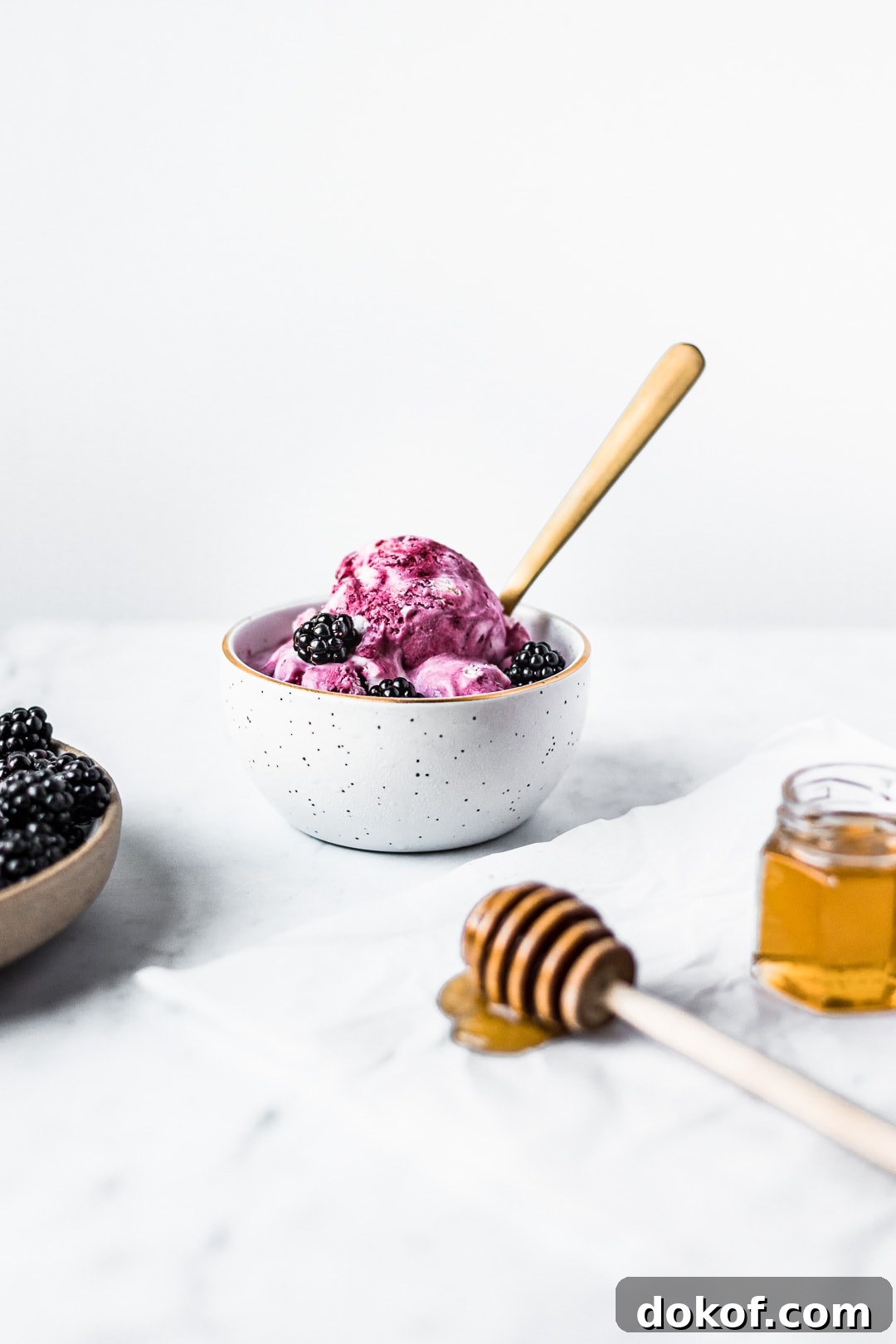 Front view of honey blackberry mascarpone ice cream scoops in a bowl with blackberries and honey in foreground