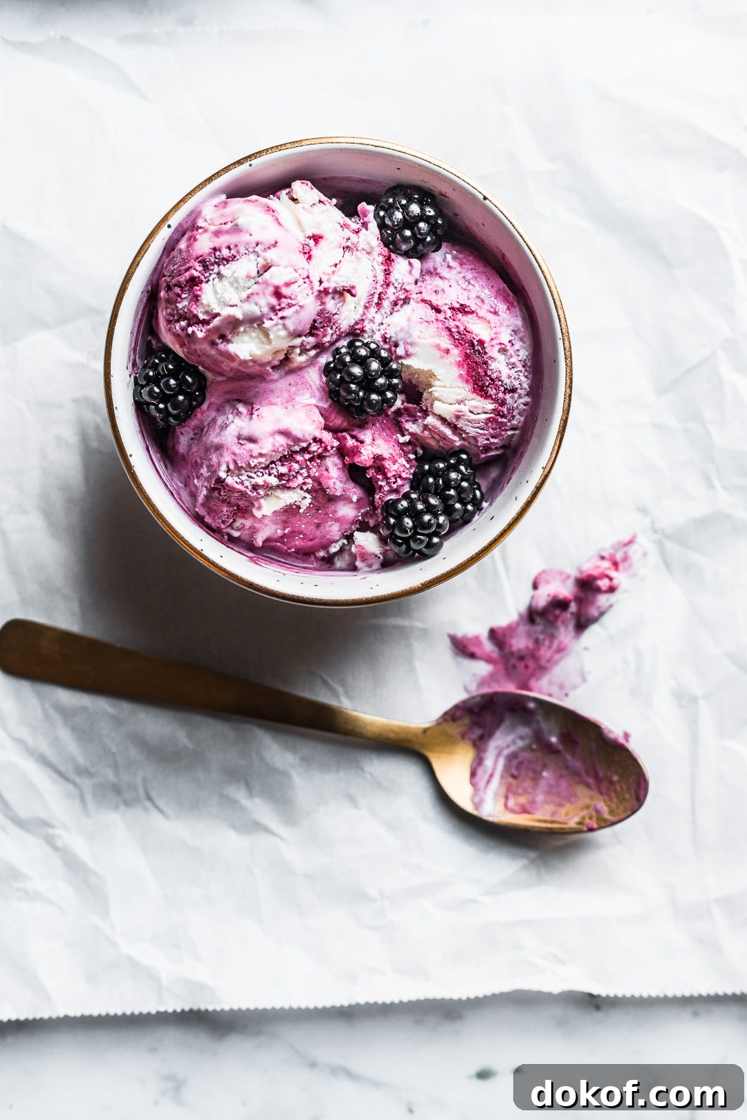 Bowl of honey blackberry mascarpone ice cream scoops with blackberries on top and gold spoon nearby