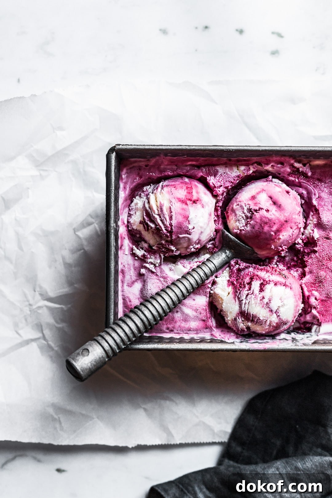 Closeup of three scoops of purple and white blackberry mascarpone ice cream in a container with the scoop resting on top