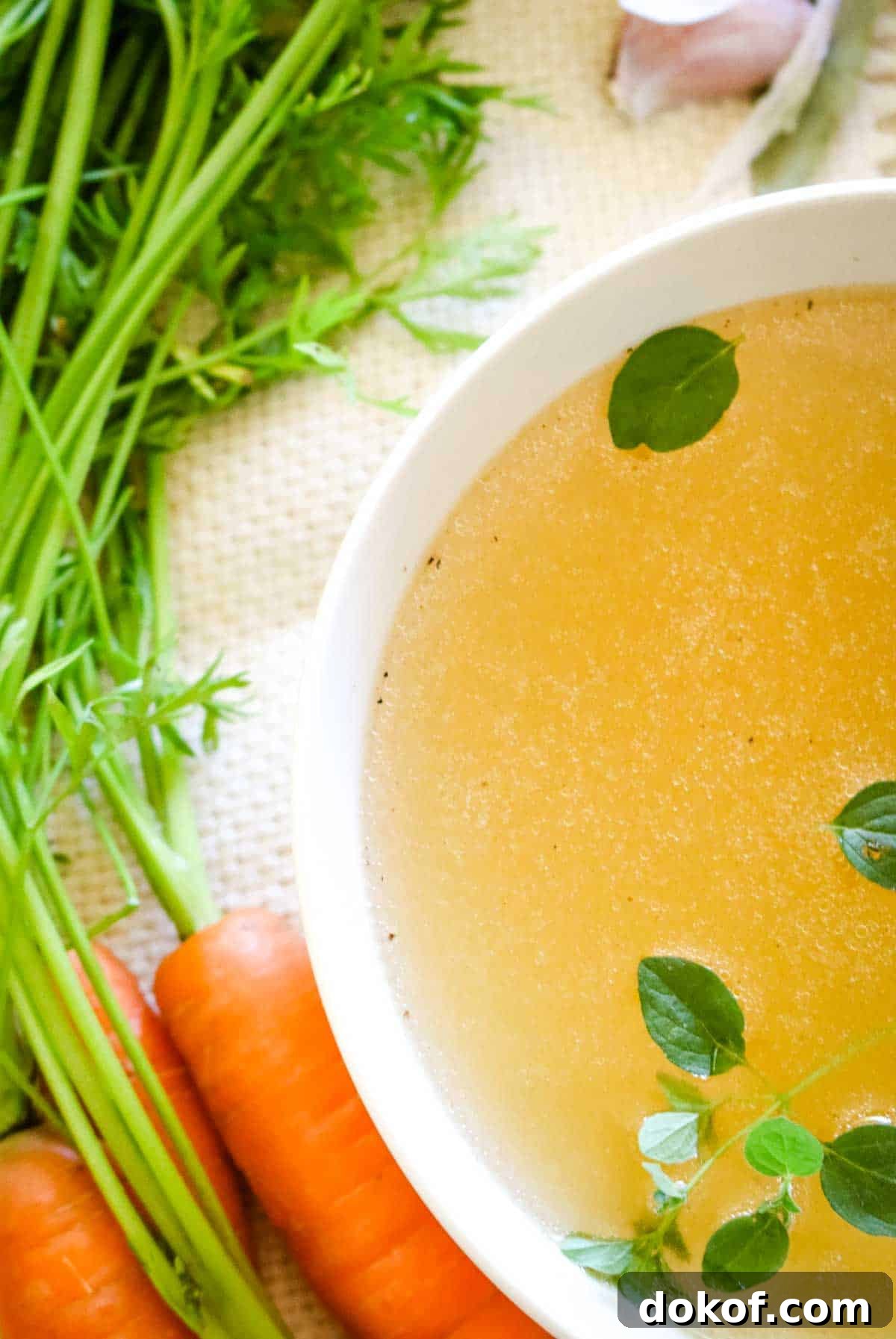 overhead of chicken bone broth with oregano leaves and carrots.