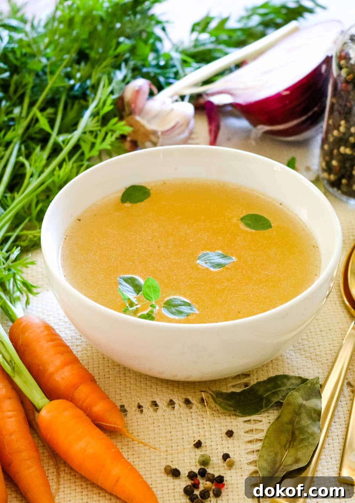 broth in white bowl with onions carrots and bay leaves.
