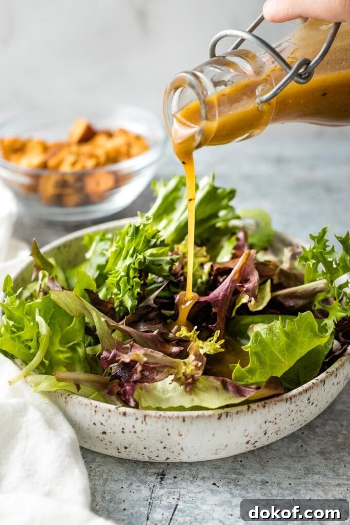 Dressing being poured on salad greens.