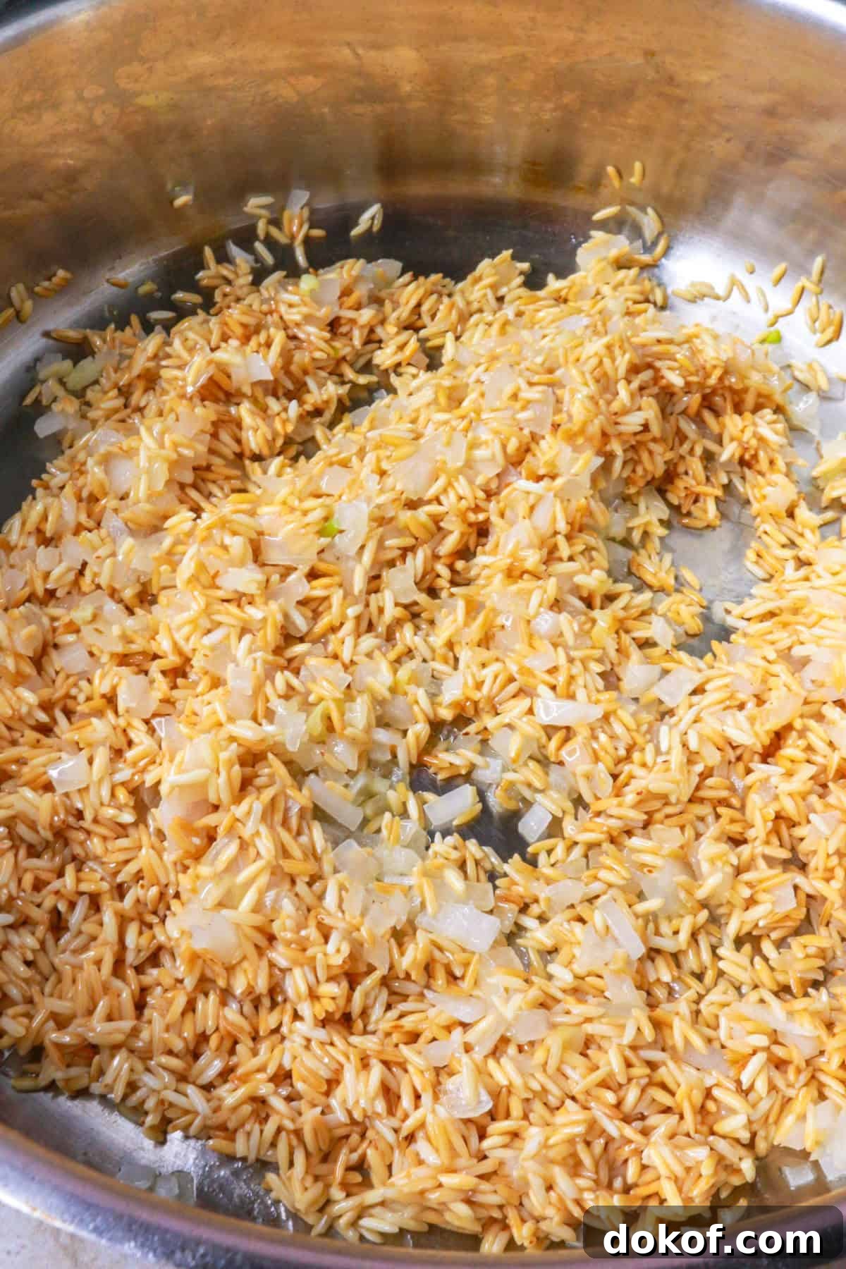 Toasted rice mixed with diced onion and garlic in a pan