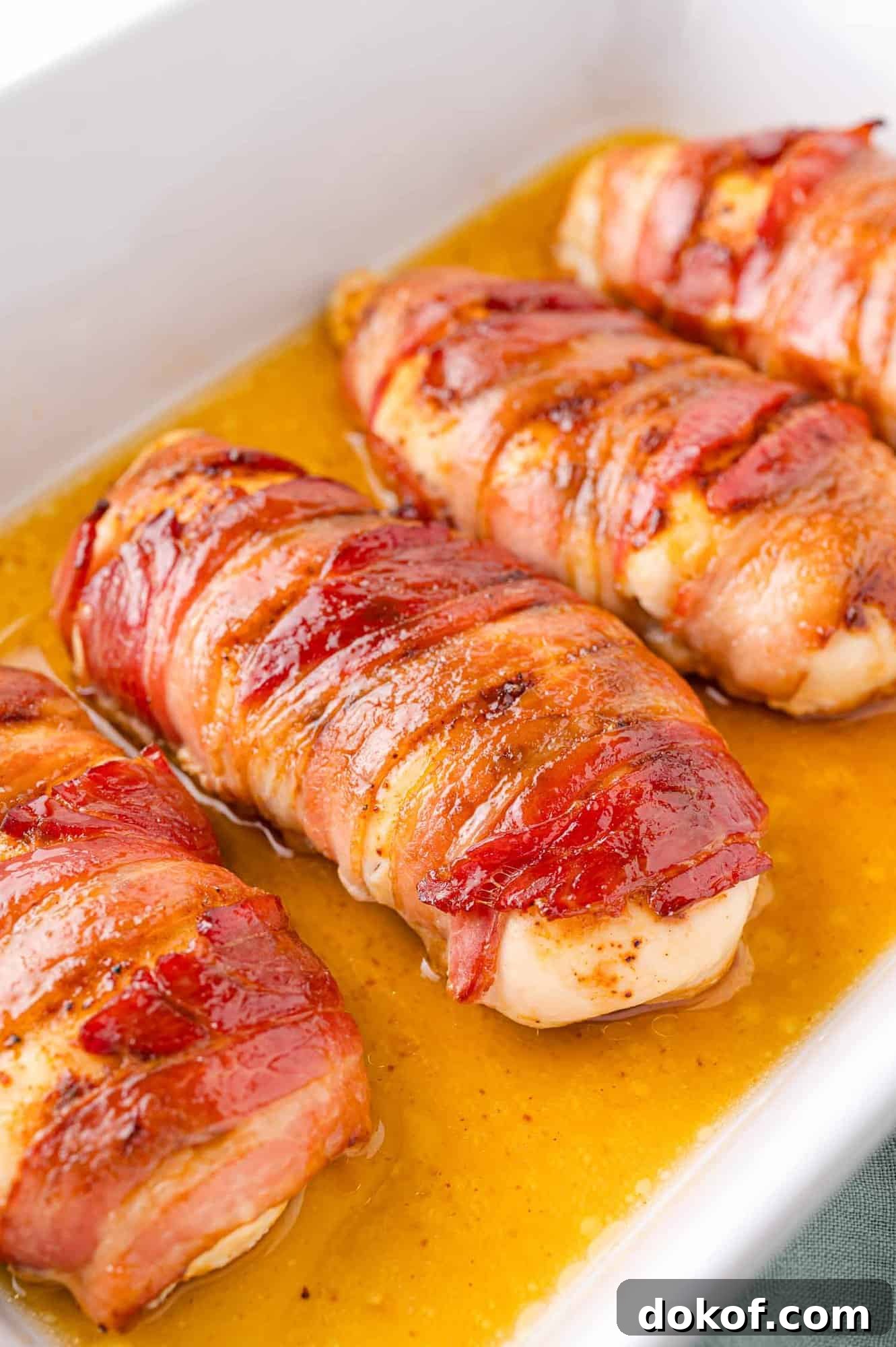 Juicy Bacon-Wrapped Chicken Breasts with Herb Butter Filling 2 Bacon-wrapped chicken breasts in a baking dish with juices visible, cooked to a golden brown.