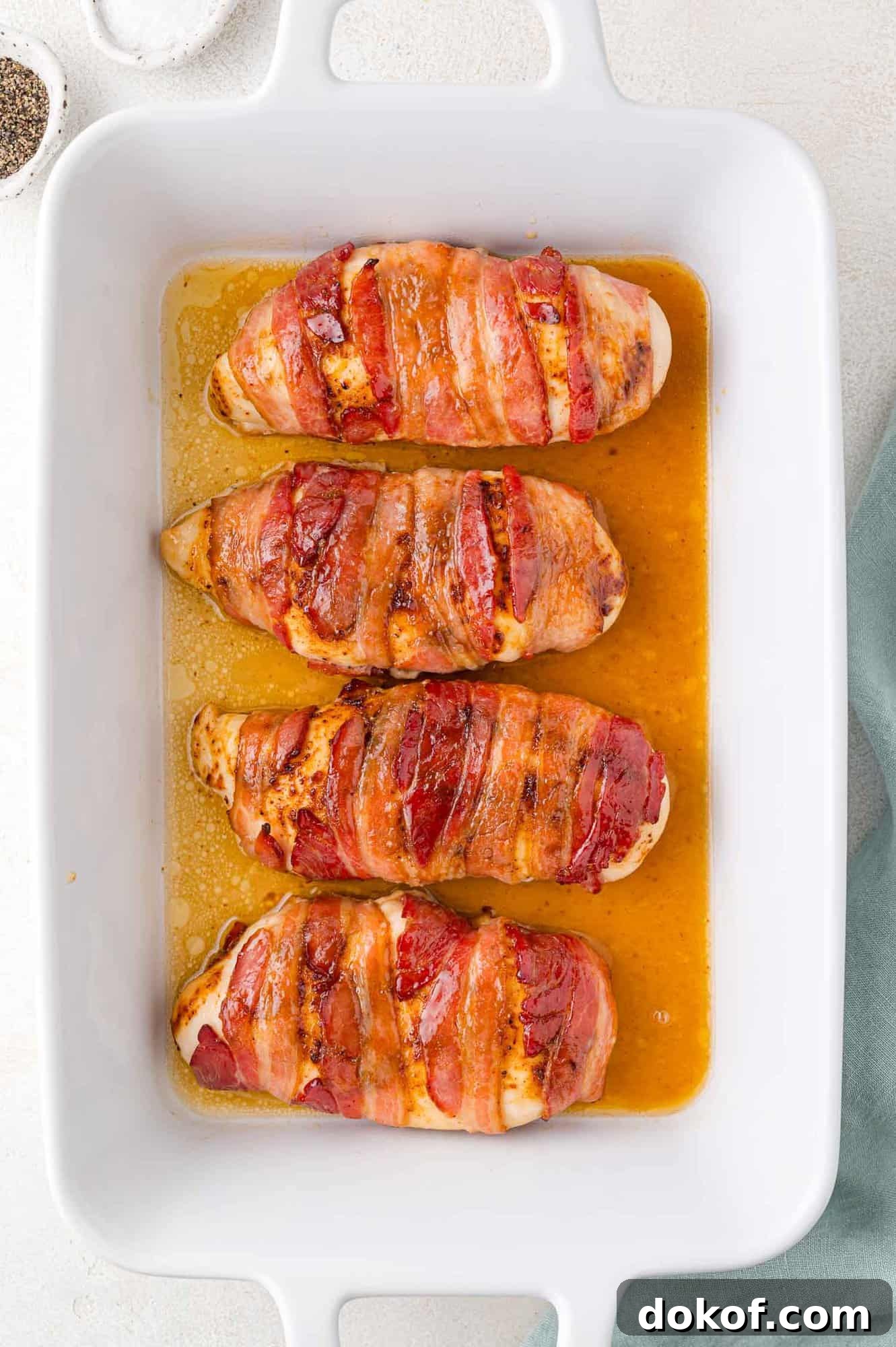 Juicy Bacon-Wrapped Chicken Breasts with Herb Butter Filling 7 Four bacon-wrapped chicken breasts in a white baking dish, cooked and browned, resting in juices.