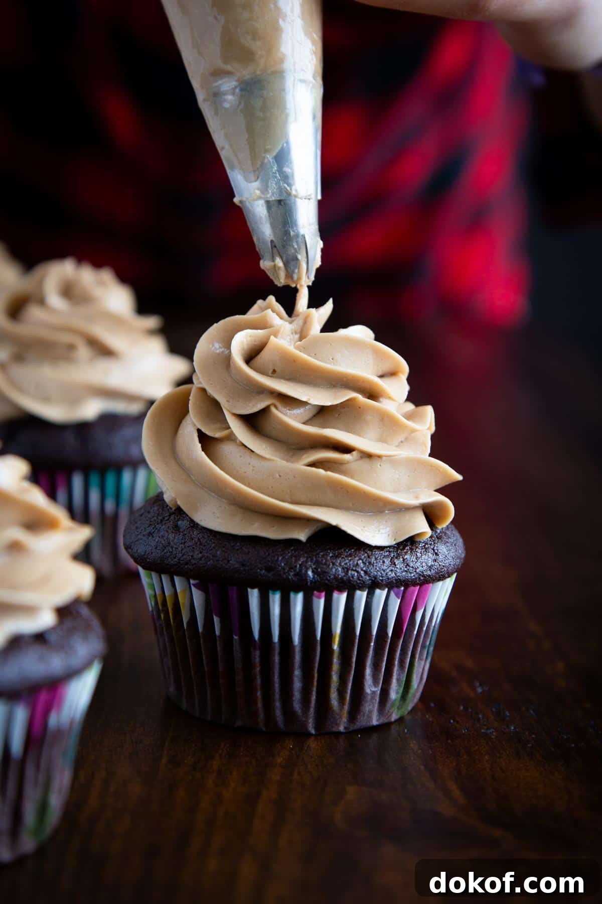 Piping coffee frosting onto a chocolate cupcake.
