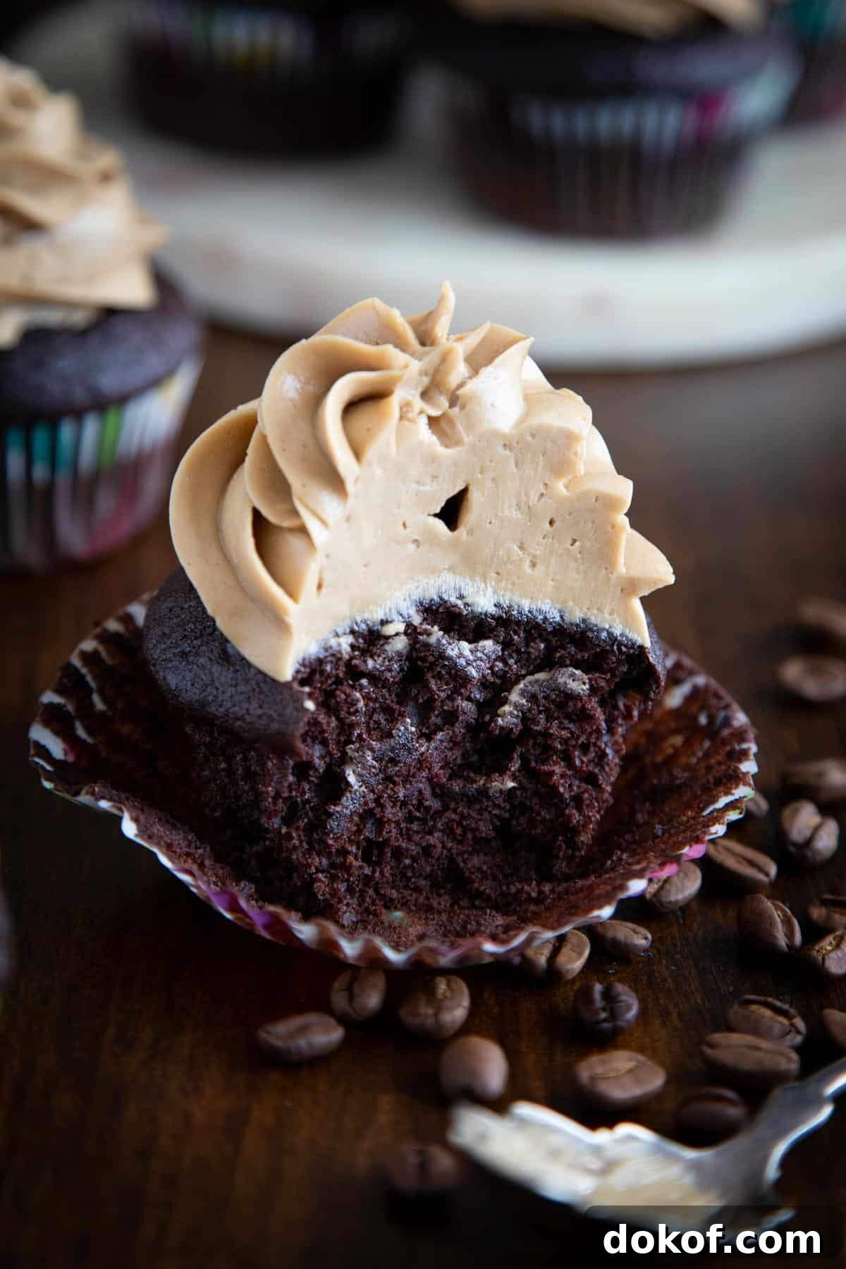 A mocha cupcake, half-eaten, next to some coffee beans.