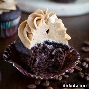 A mocha cupcake, half-eaten, next to some coffee beans.