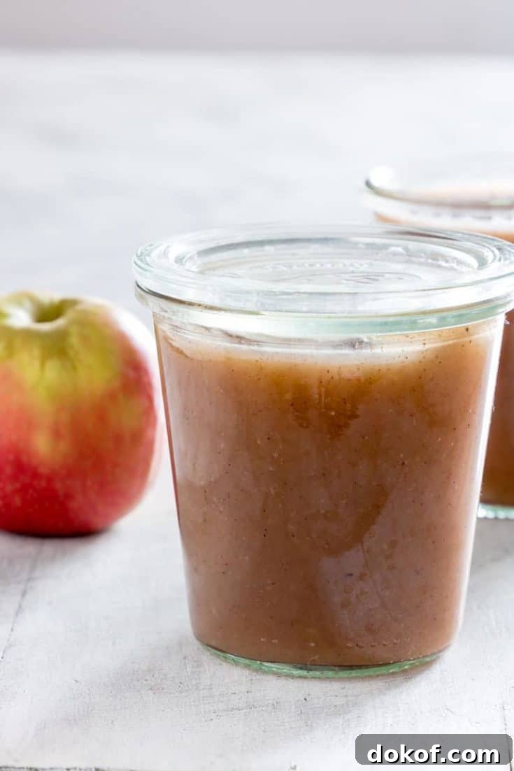 A jar full of Instant Pot Applesauce with apple and another jar in the background