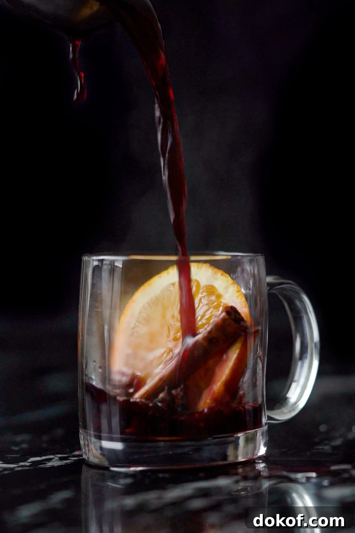 Pouring a refined sugar free keto mulled wine onto a glass mug with an orange slice and cinnamon stick 