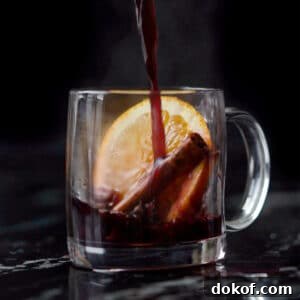 Pouring a refined sugar free keto mulled wine onto a glass mug with an orange slice and cinnamon stick