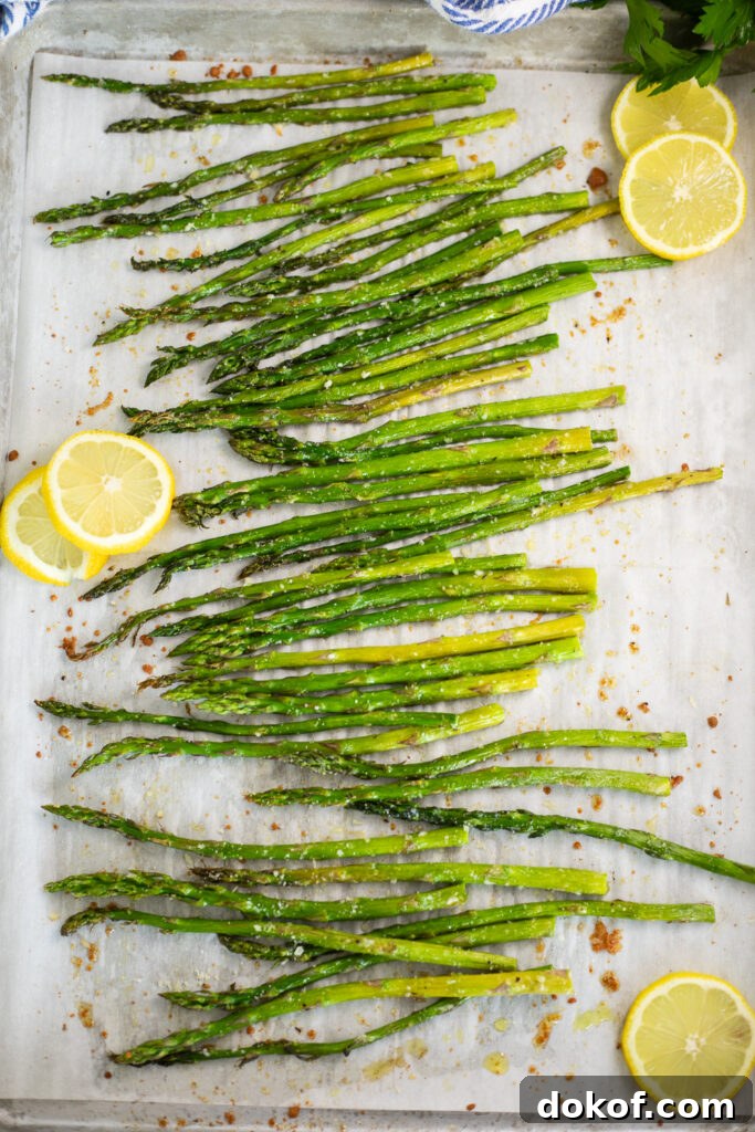 Crispy Oven-Roasted Asparagus with Garlic and Parmesan 2 Oven roasted asparagus and lemon slices on a baking sheet lined with parchment paper.