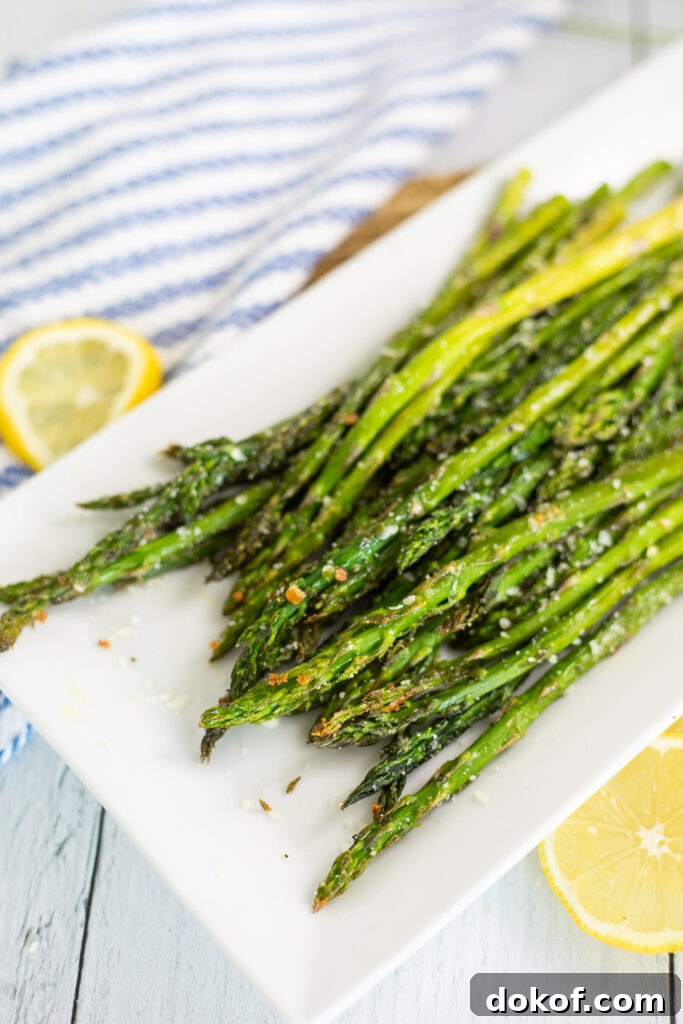 Crispy Oven-Roasted Asparagus with Garlic and Parmesan 3 Oven roasted asparagus on a white rectangular plate next to lemon slices.