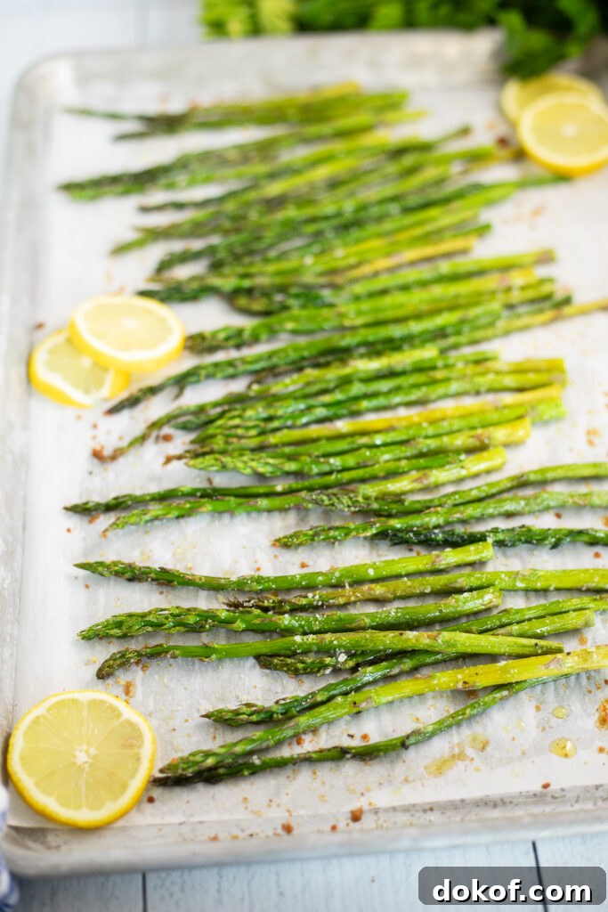 Crispy Oven-Roasted Asparagus with Garlic and Parmesan 4 Oven roasted asparagus and lemon slices on a baking sheet lined with parchment paper.