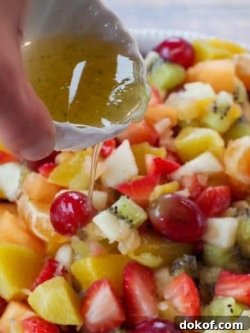 easy fruit salad in white bowl with honey lime dressing being poured over salad