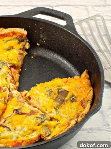 healthy breakfast pizza in cast iron pan with one piece missing and utensil (lifter) on the side