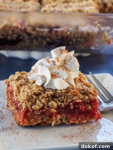 rhubarb square on a white plate, with glass dish of more rhubarb squares in the background