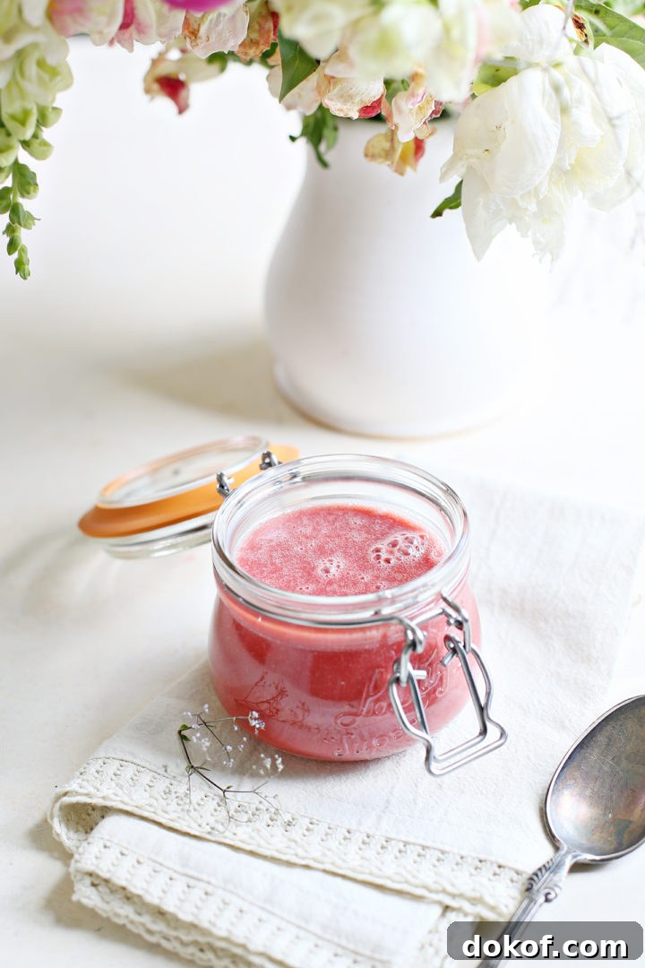 jar of raspberry curd on a white counter with a vase of flowers