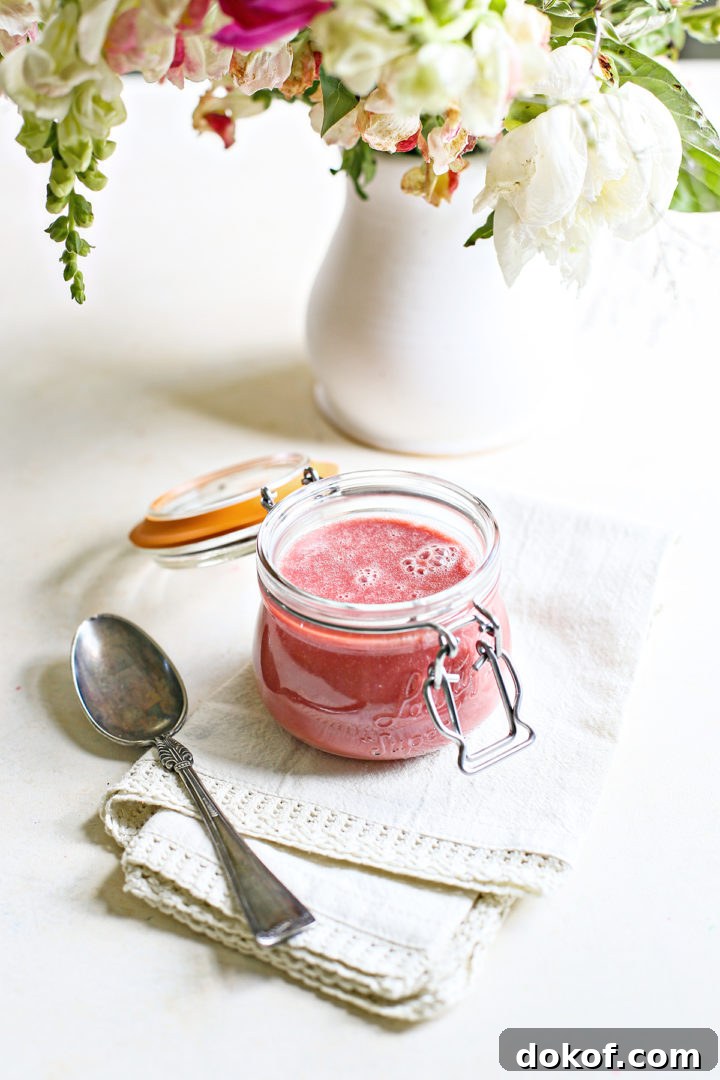 raspberry curd in a jar on a white counter with a spoon and vase of flowers
