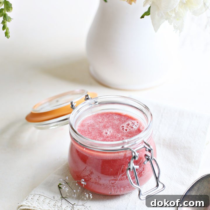 a jar of raspberry curd on a white counter with a vase of flowers