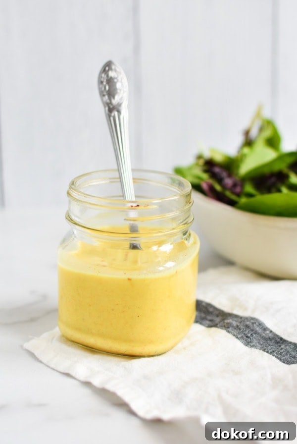 A yellow curry dressing in a mason jar with a spoon