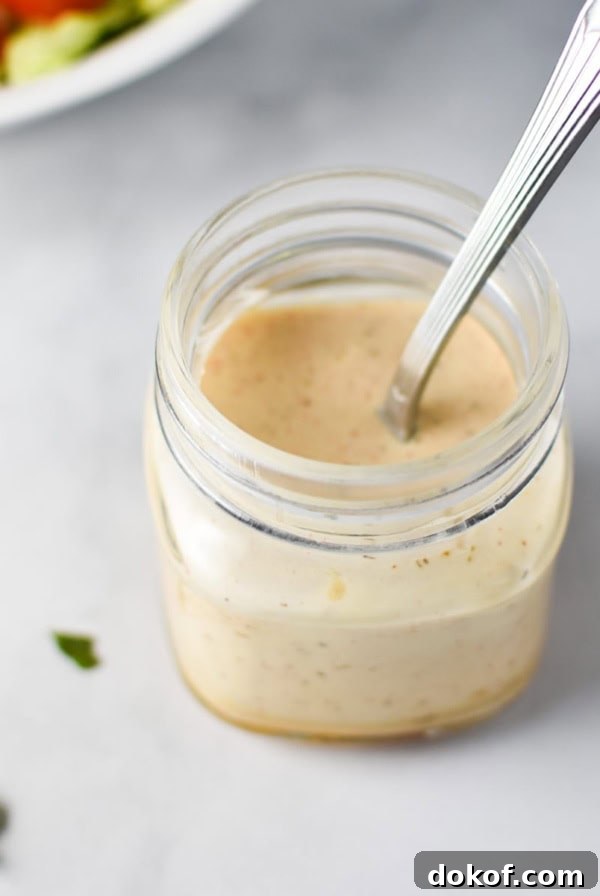 A mason jar with honey mustard ranch and a spoon inside with chopped parsley on top