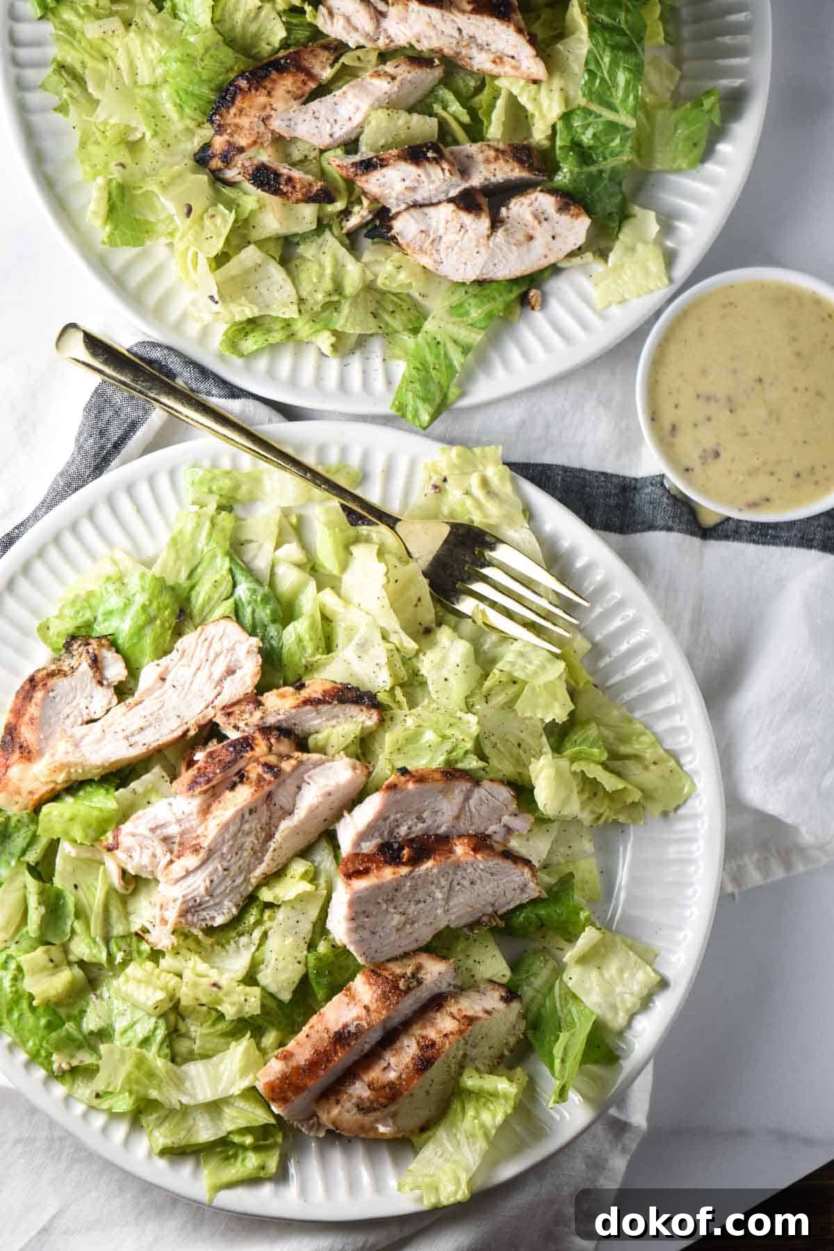 Two Caesar salads next to a bowl of homemade Caesar salad dressing.