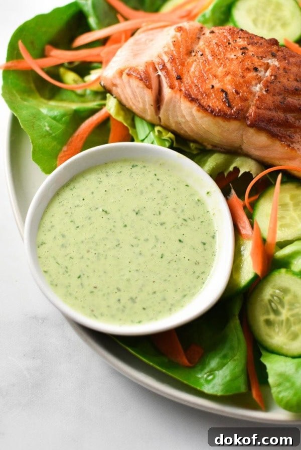 A bowl of creamy basil dressing next to seared salmon on a green salad