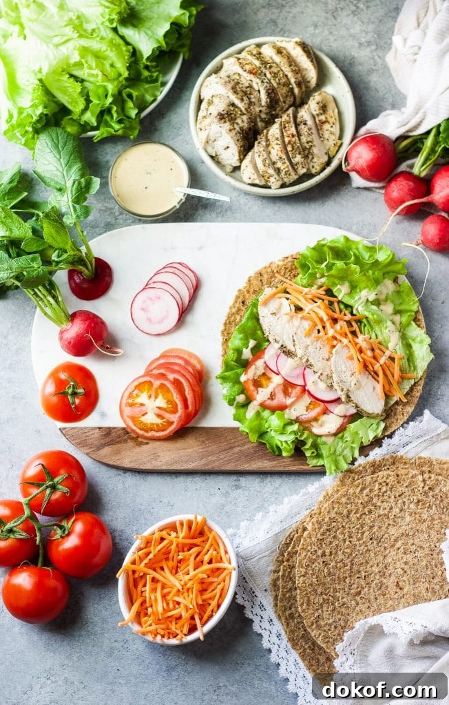 Chicken Caesar Wrap Recipe: Quick Protein-Packed Lunch 4 Assembling the wrap on a chopping board with chicken sliced tomatoes, radishes, cheese, lettuce and Caesar dressing.