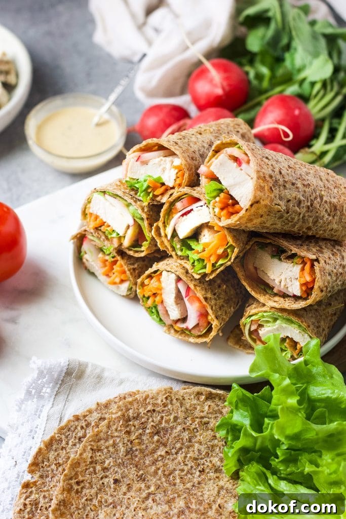Chicken Caesar Wrap Recipe: Quick Protein-Packed Lunch 7 Healthy chicken Caesar wraps stacked on a white plate with radishes, tomato, wraps, and Caesar dressing in the background.